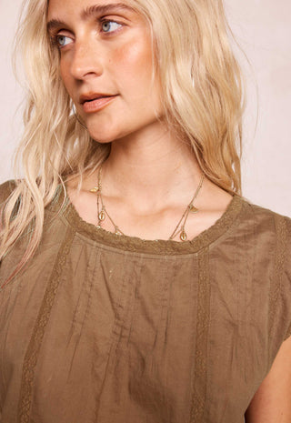 a-close-up-of-a-blonde-woman-wearing-a-brown-textured-top-with-lace-trim-and-layered-gold-necklaces